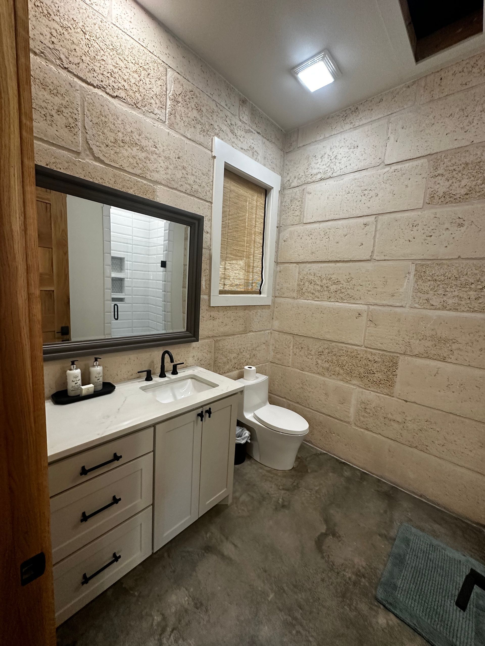 A bathroom with a sink , toilet , mirror and brick walls.