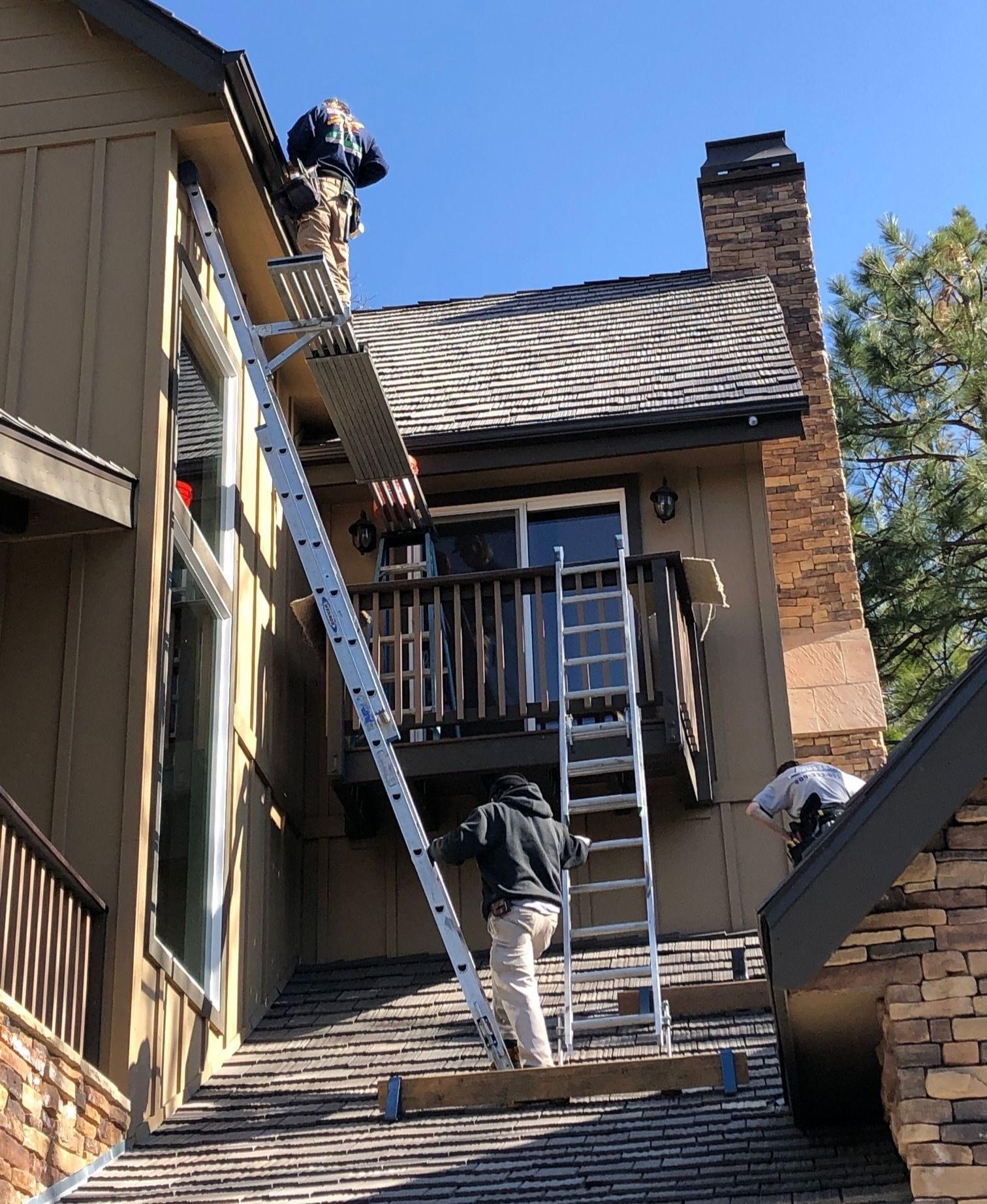 A man is standing on a ladder on the roof of a house.