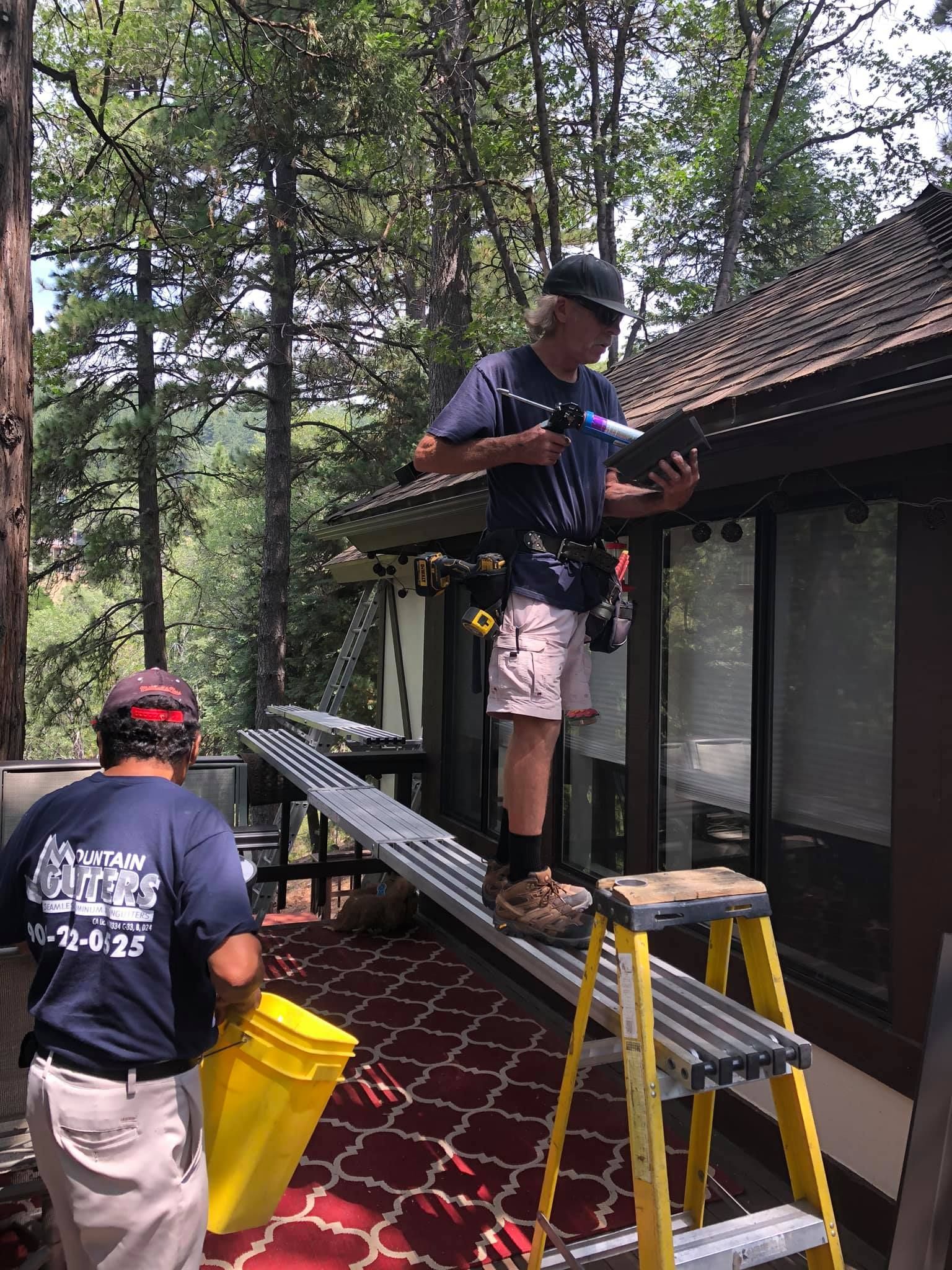 A man is standing on a ladder working on the roof of a house.