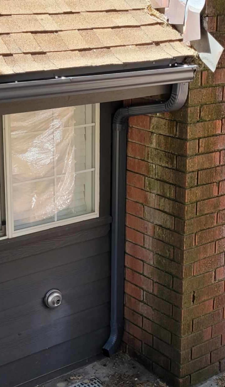 A gutter is attached to the side of a brick building next to a window.