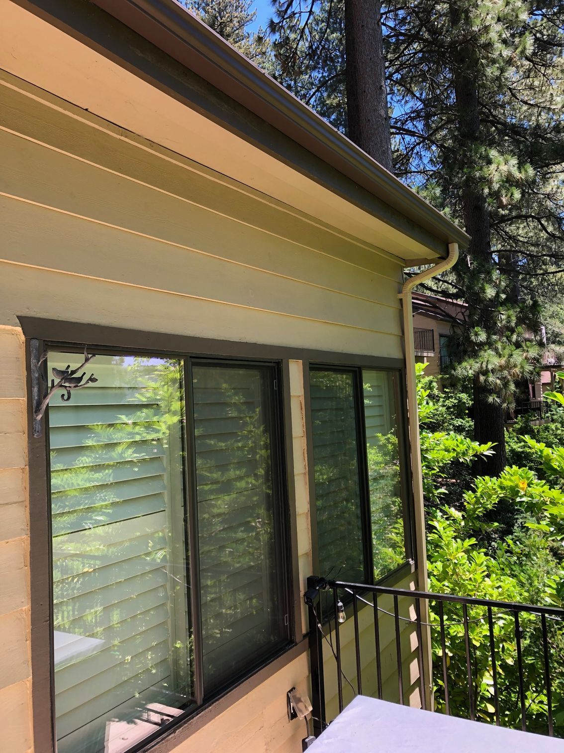 A house with a large window and a balcony with trees in the background.