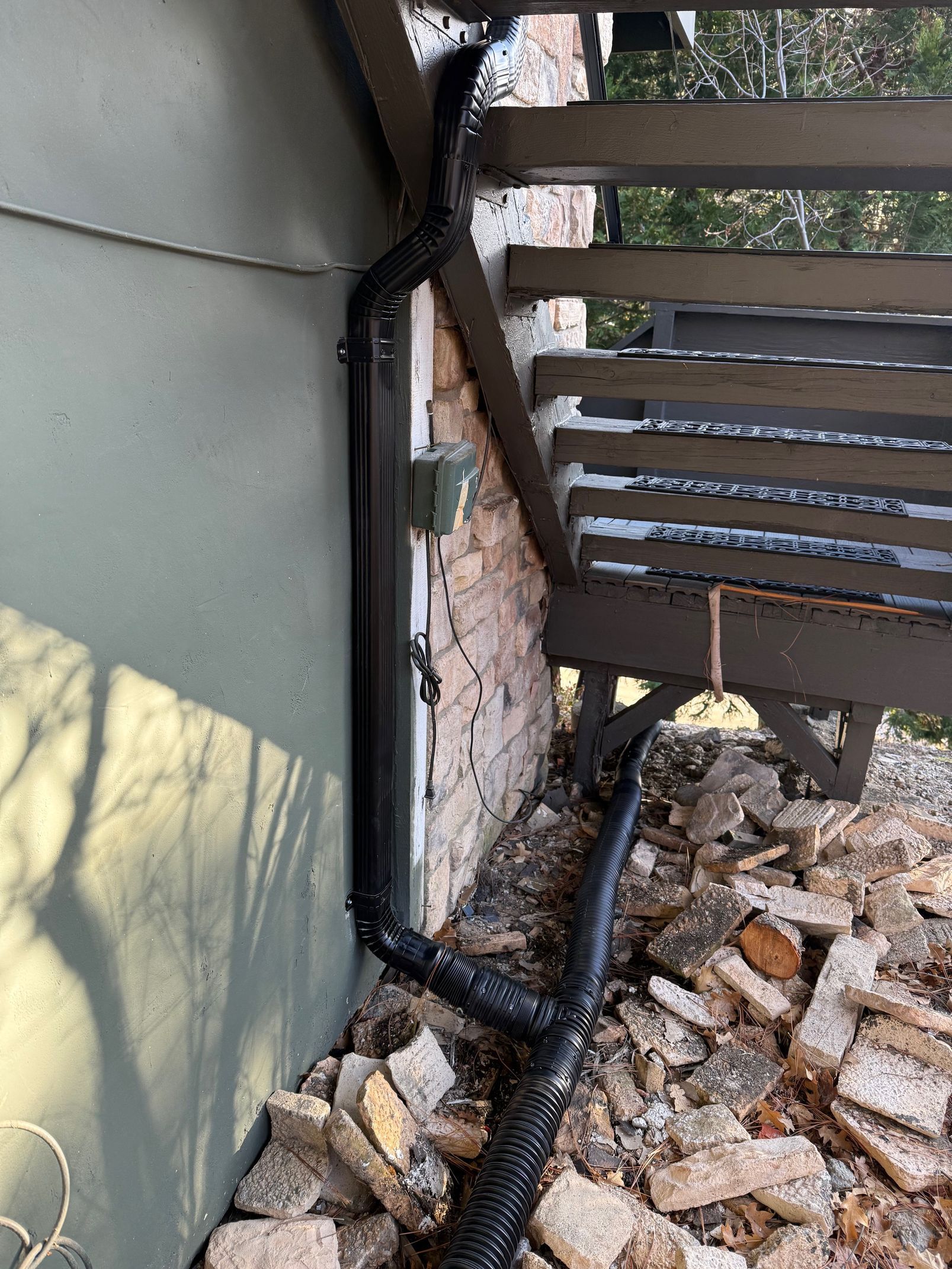 A black pipe is coming out of the side of a building next to a wooden railing.