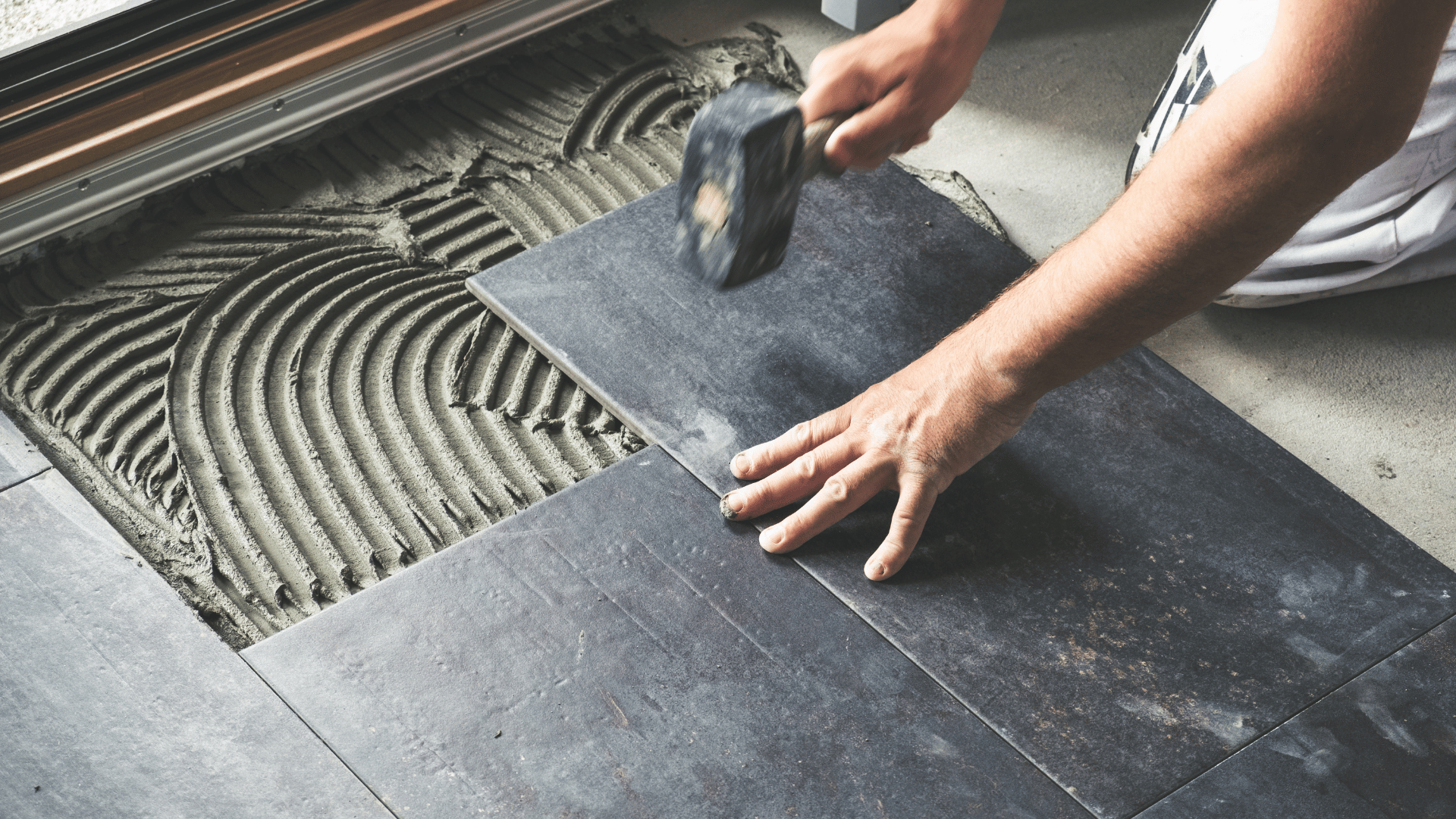 A person is laying tiles on the floor with a hammer.