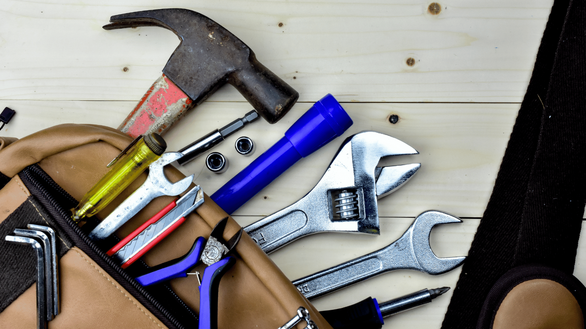 A tool bag filled with tools and a hammer on a wooden table.
