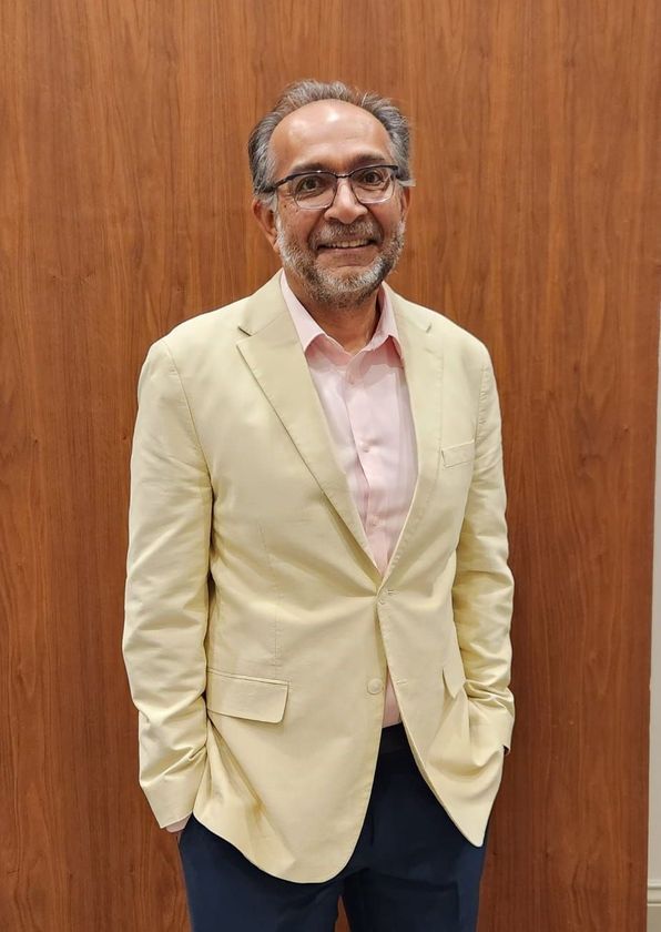 A man in a suit and glasses is leaning on a railing and smiling.