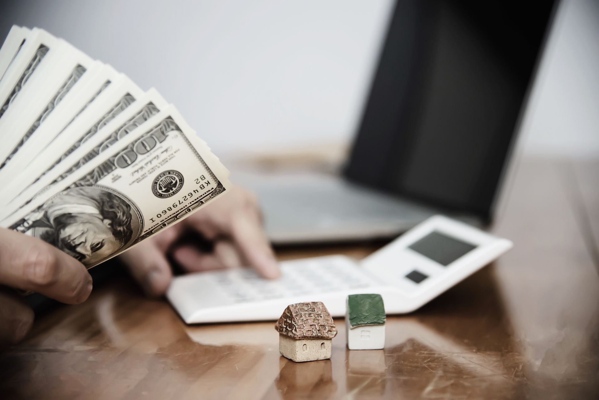 A person is holding a stack of money in front of a laptop.