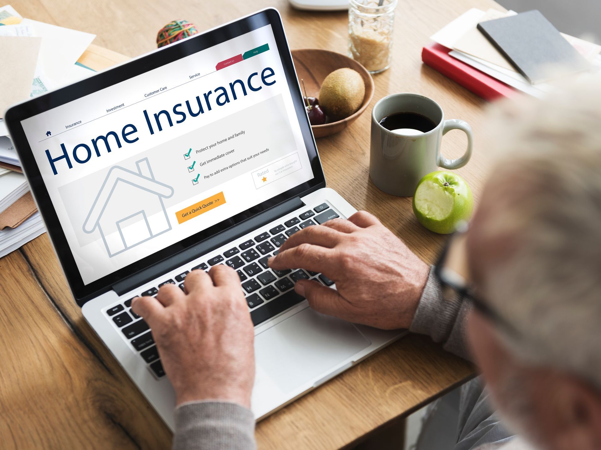 A man is typing on a laptop computer with a home insurance website on the screen.