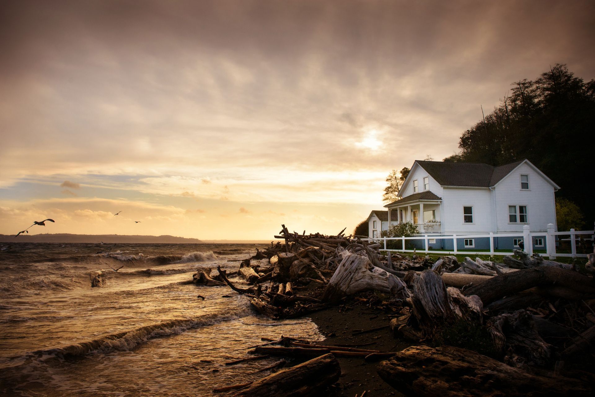 A white house is sitting on the shore of a body of water at sunset.