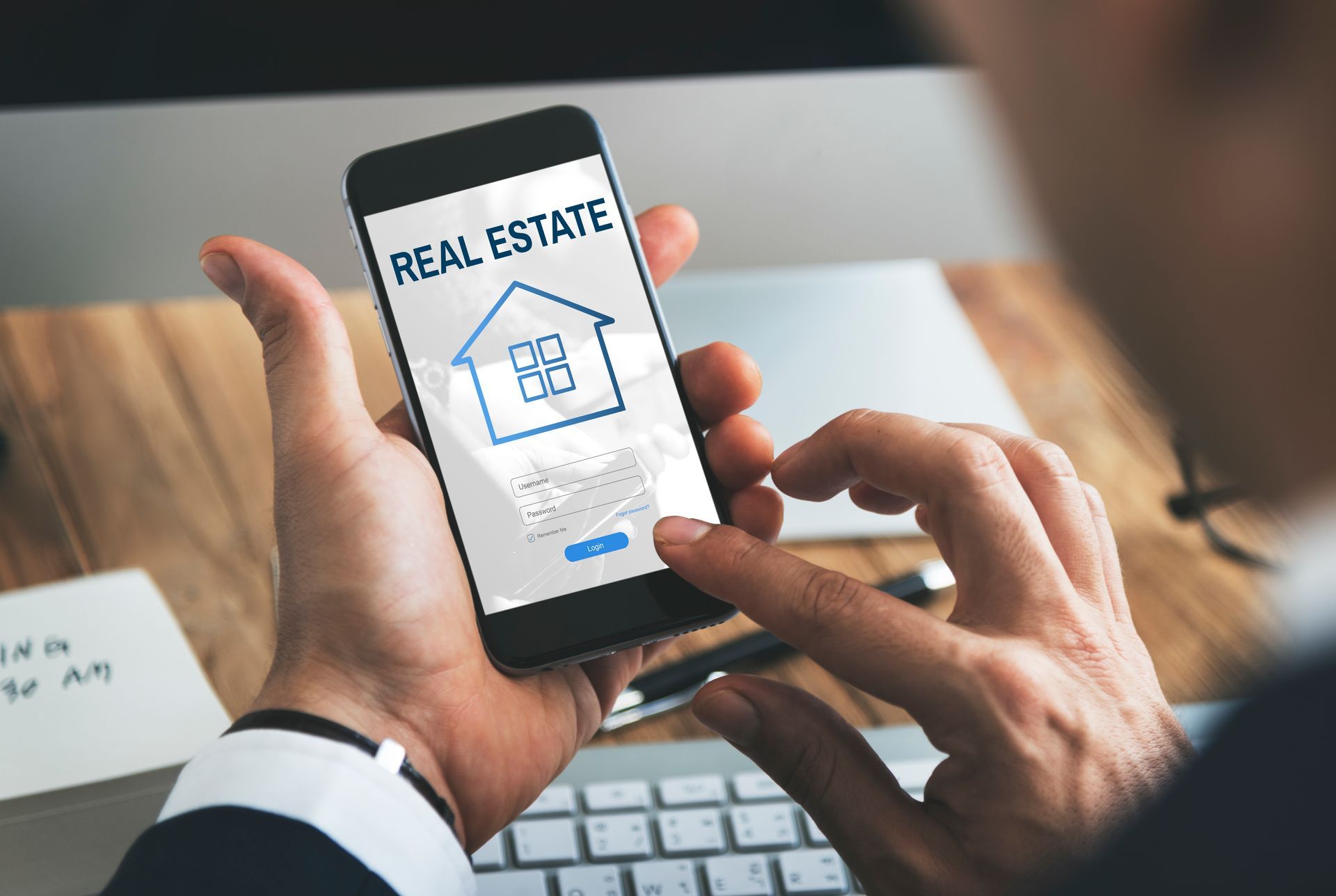 A man is holding a cell phone with the word real estate on the screen.