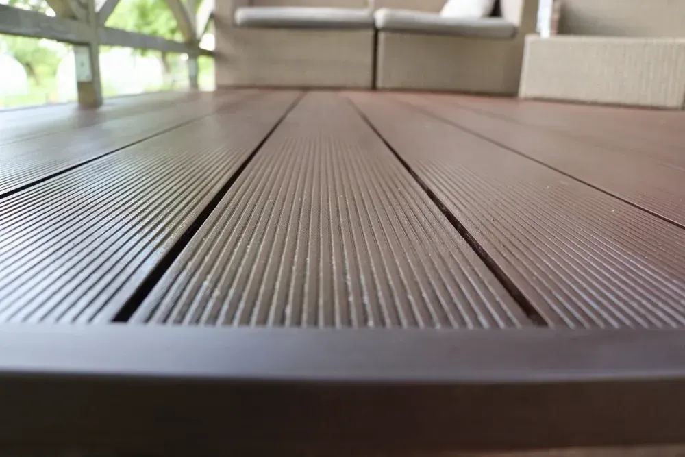 Close-up of a brown composite deck with textured grooves; outdoor seating in the background. — Dimond J Carpentry in Sunshine Coast, QLD