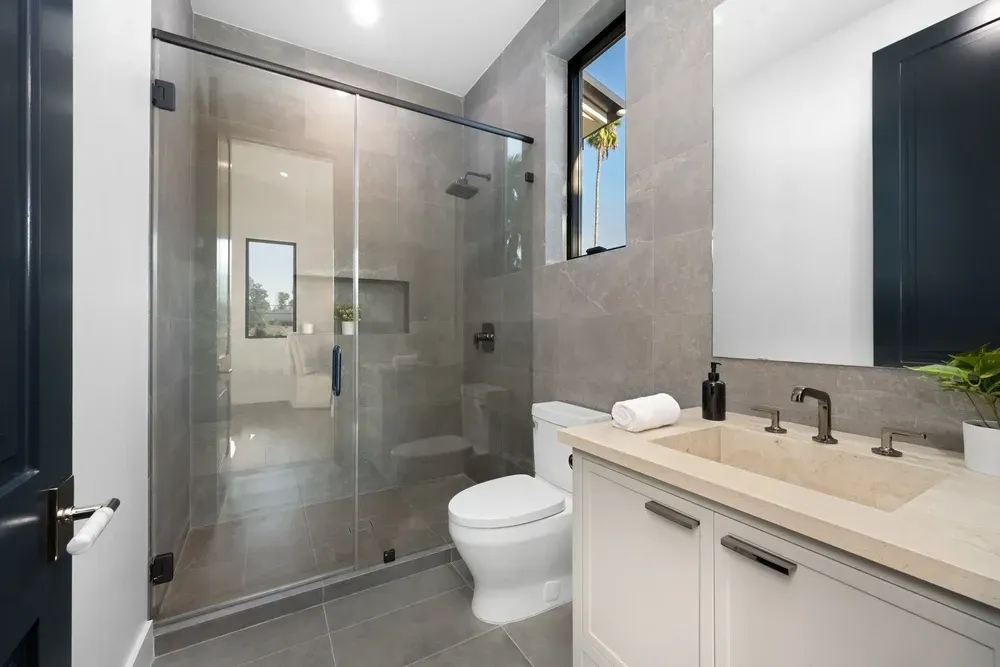 Modern bathroom with a glass shower, white vanity, and gray tile walls. — Dimond J Carpentry in Bli Bli, QLD