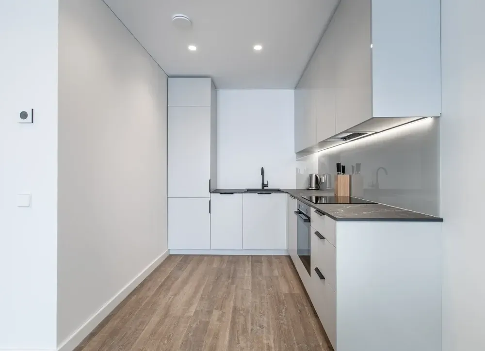 Modern, white kitchen with wood-look flooring, stainless steel appliances, and a corner layout. — Dimond J Carpentry in Sunshine Coast, QLD