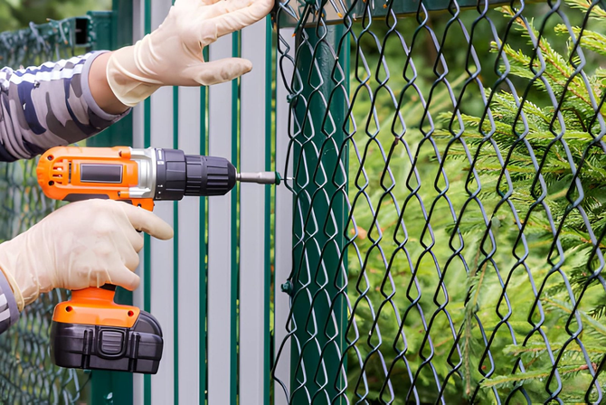 Worker installing green chain link fence