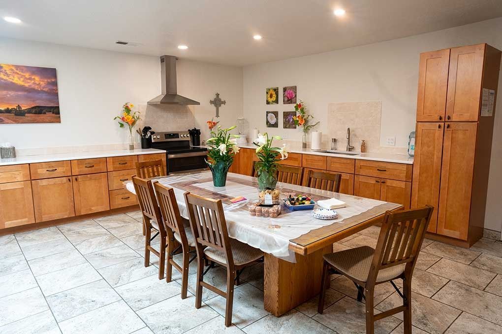 Kitchen with long wooden table set for meal, wooden cabinets, stainless steel appliances, and tile floor.