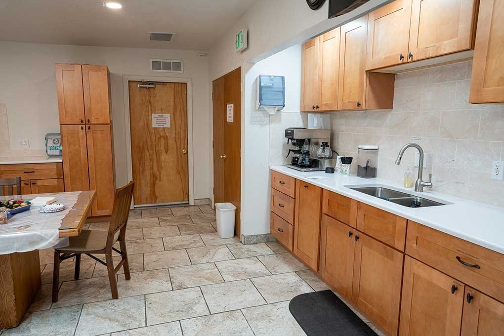 Kitchen with light wood cabinets, stainless steel sink, and beige tile floor.