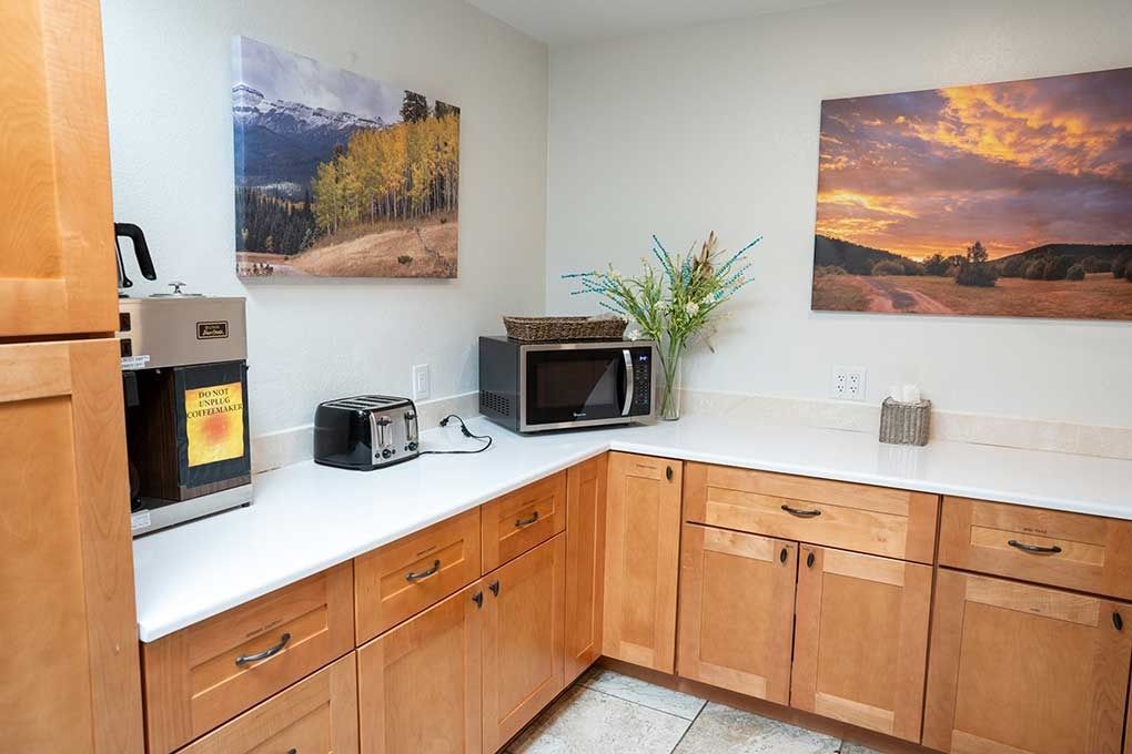 Kitchenette with light wood cabinets, white countertops, microwave, toaster, and artwork.