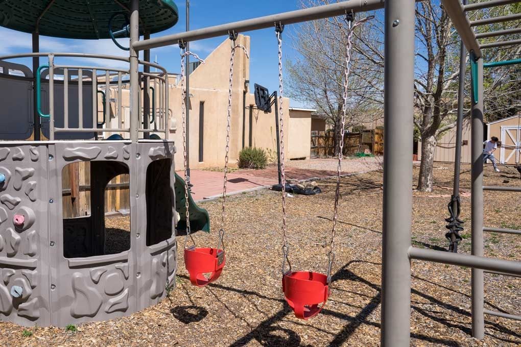 Playground with two red bucket swings, climbing structure, and building in the background.