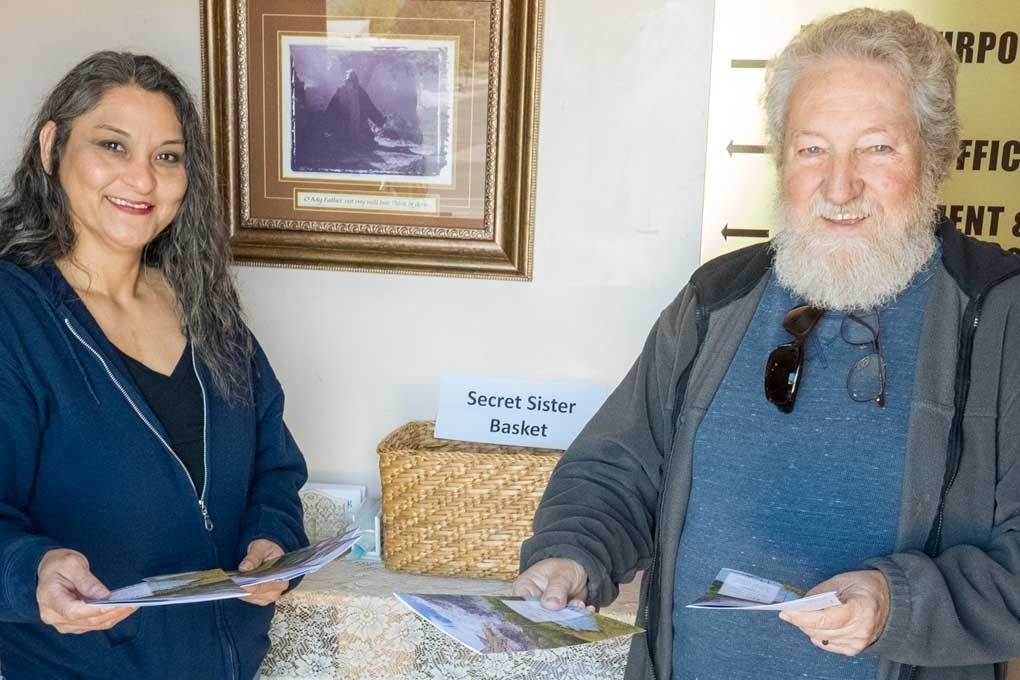 Woman and man smiling, holding papers near a 