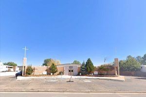 Church with a cross on a blue sky day. Concrete building with a cross. Trees line the entrance.