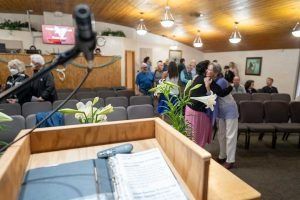 People in church: two women hugging, preacher's podium, rows of seats.
