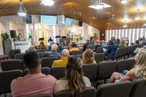 People seated in a church, listening to a presentation on stage.