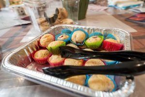 Mini muffins in colorful liners, tongs in a foil tray.