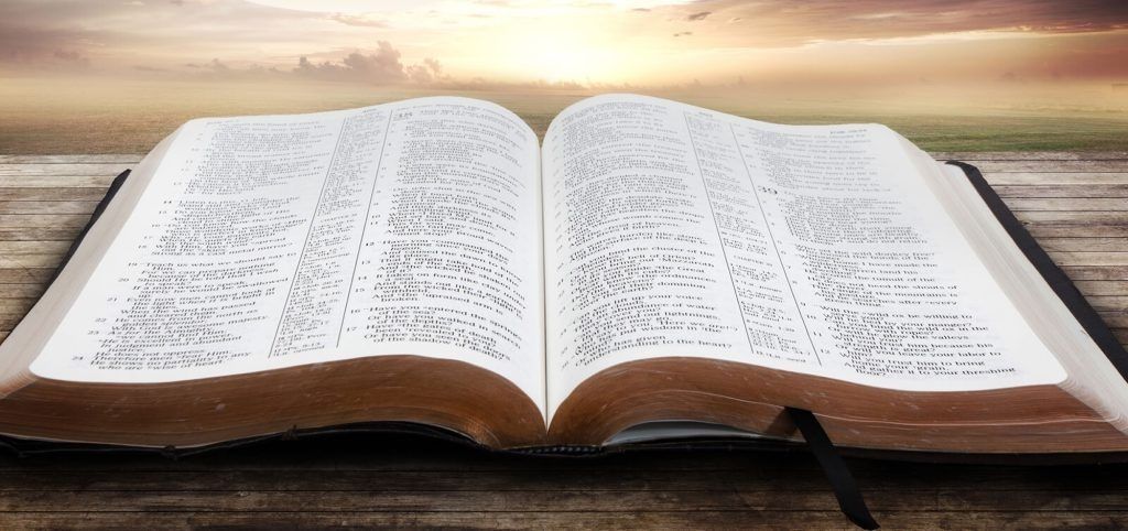 Open Bible on a wooden surface, with a sunset background.