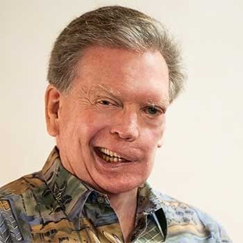 Man with light skin and a wide smile wearing a patterned shirt.