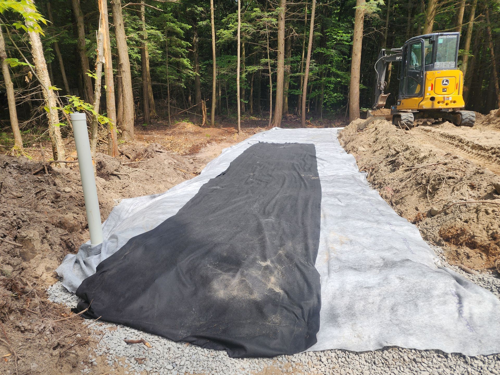Une excavatrice jaune travaille sur un chemin de terre dans les bois.