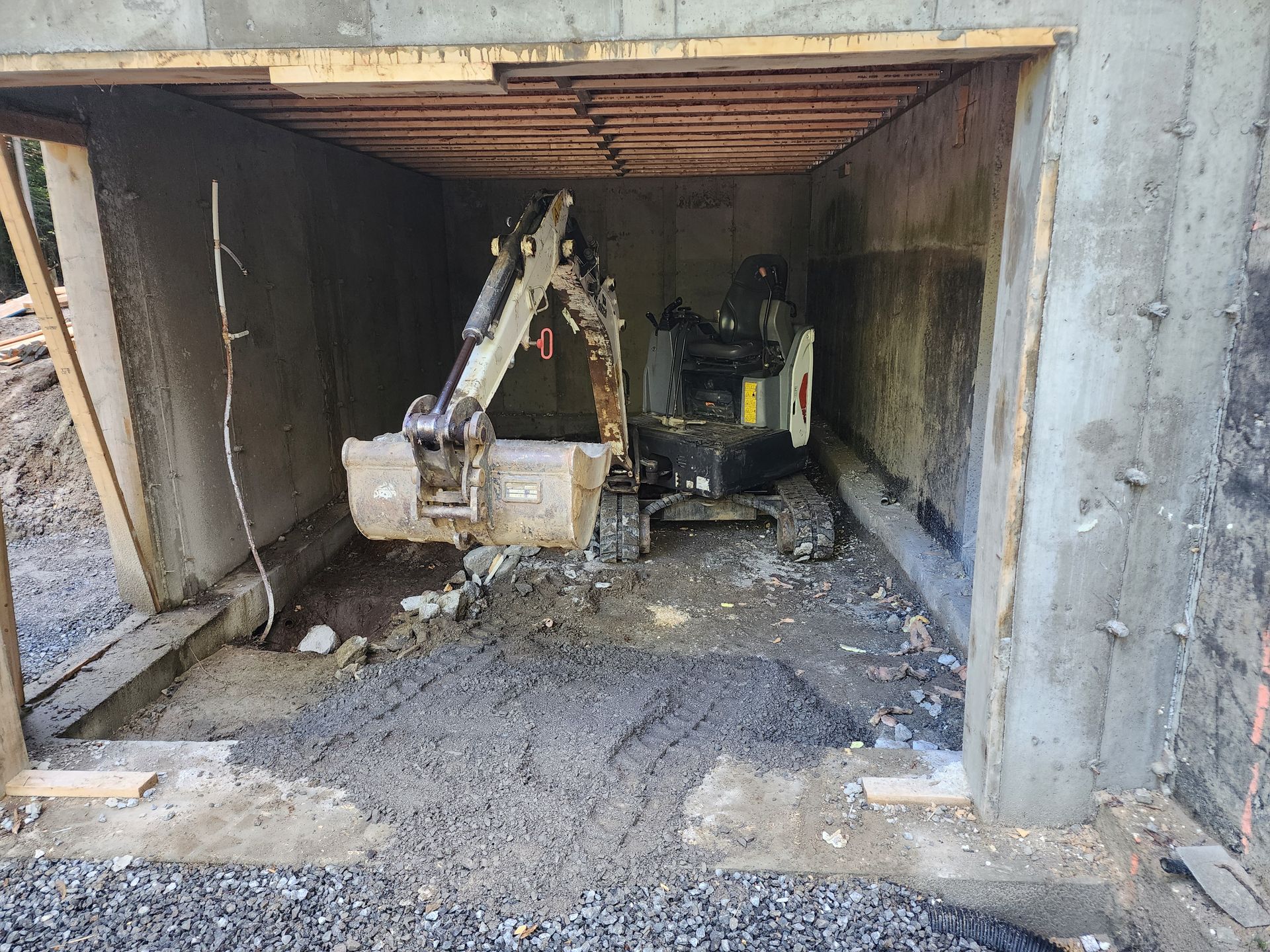 Une petite excavatrice est assise à l'intérieur d'un garage en construction.