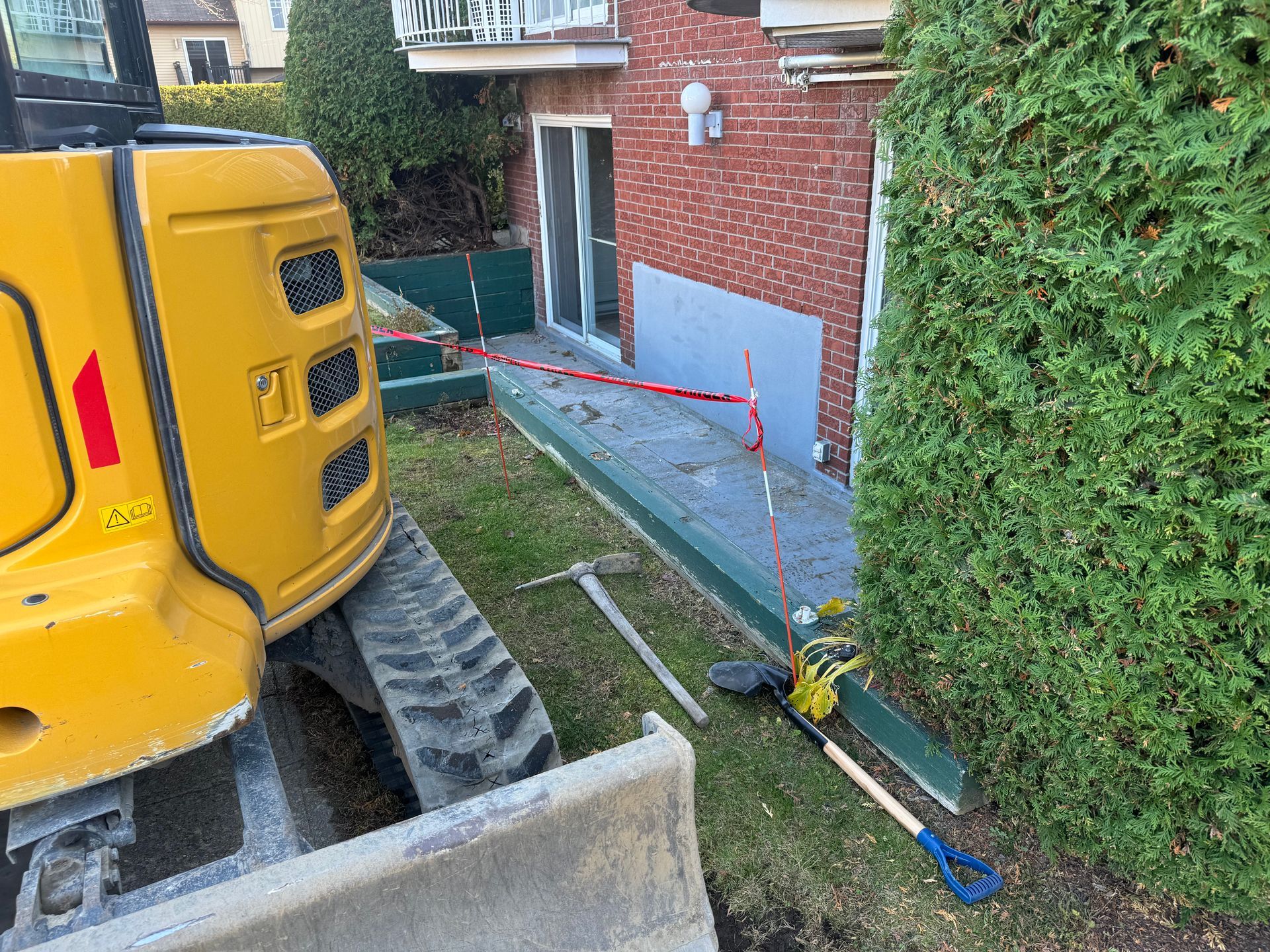 Une excavatrice jaune est garée devant une maison en briques.