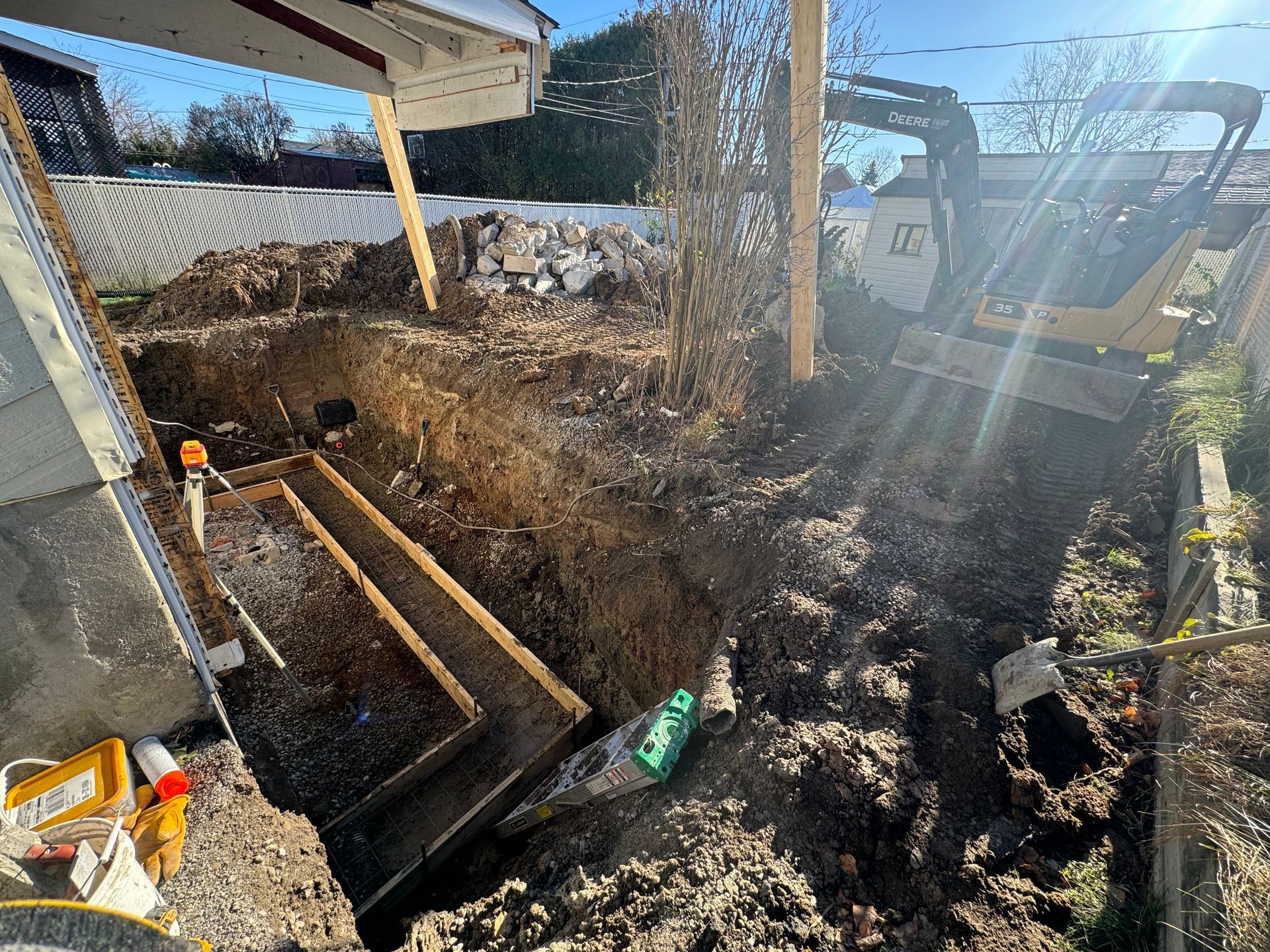 Une excavatrice creuse un trou dans le sol devant une maison.