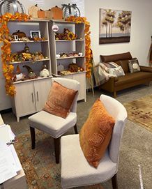Chairs with orange pillows in front of shelves decorated for fall. A couch and art are in the background.