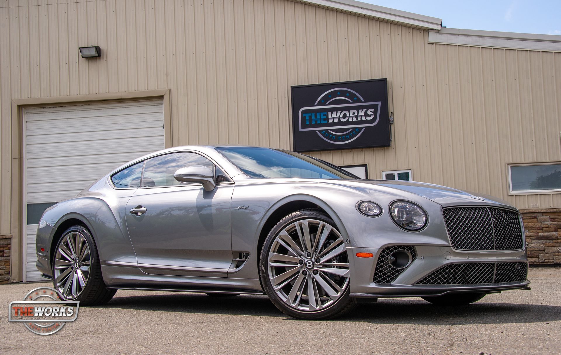 A silver bentley continental gt is parked in front of a building.