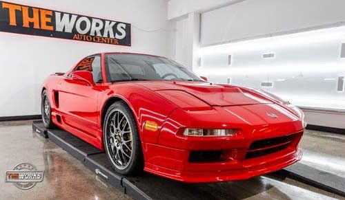 A red sports car is parked in front of a sign that says the works auto center.