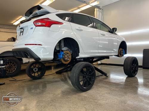 A white ford focus is sitting on a lift in a garage.