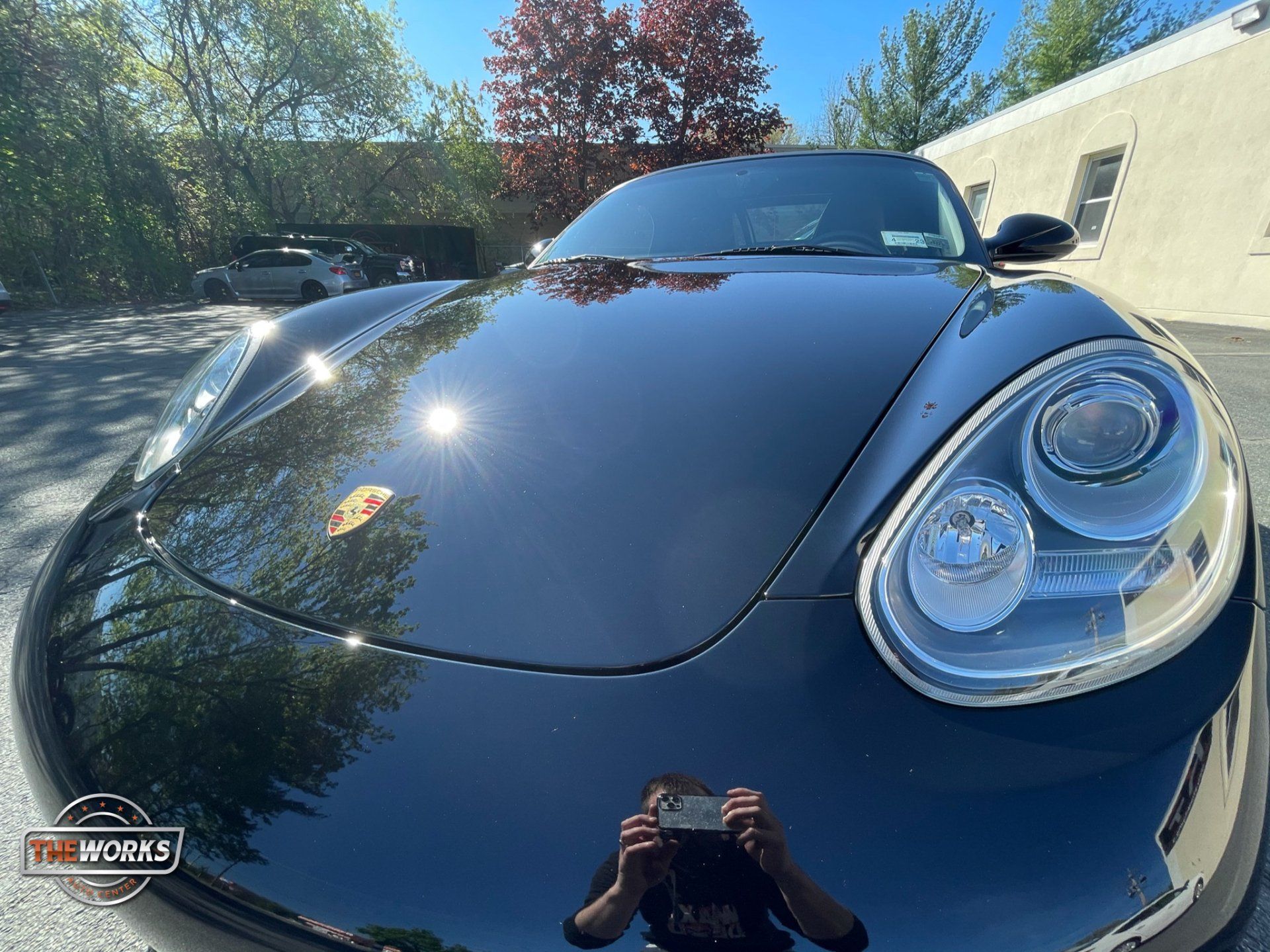 A man is taking a picture of his reflection in the hood of a black sports car.