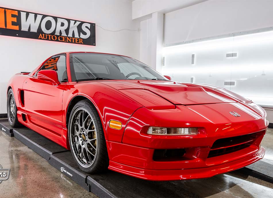 Red Honda NSX sports car on a service ramp in an auto repair shop.