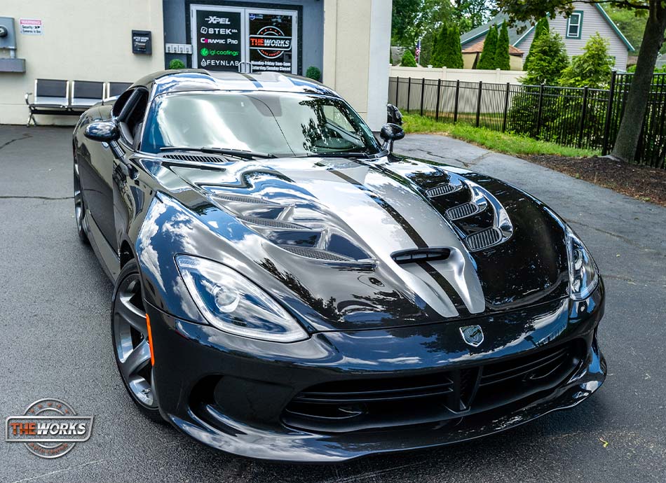Black Dodge Viper sports car with silver racing stripes parked in front of a shop.