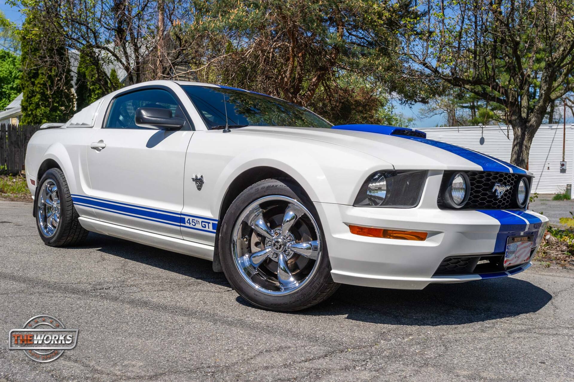 A white and blue ford mustang is parked on the side of the road.