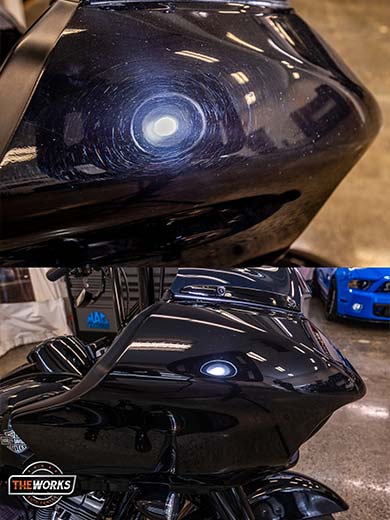 A black motorcycle is parked in a garage next to a blue car.