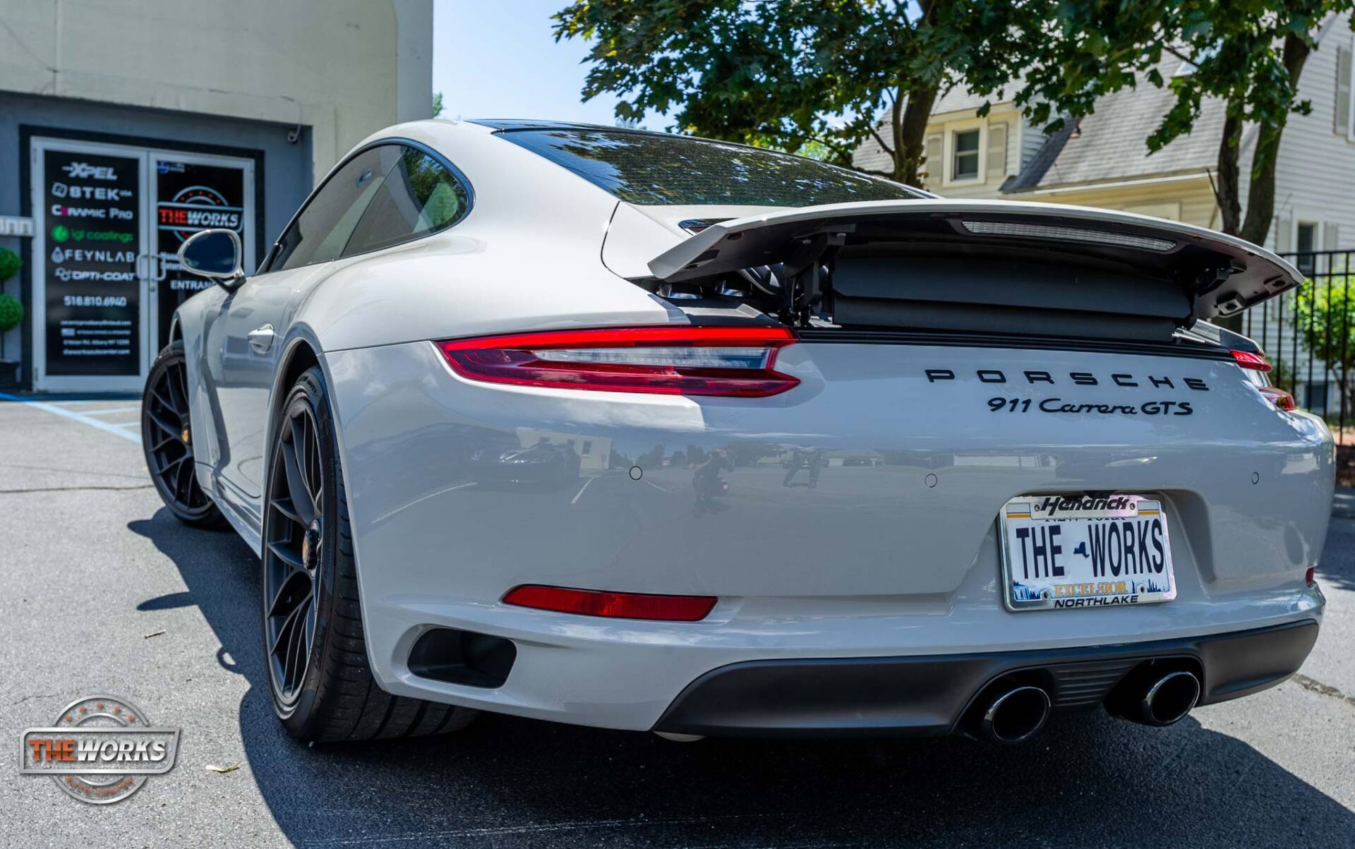 Gray Porsche 911 Carrera GTS parked outside a building. Rear view shows spoiler, black wheels, and