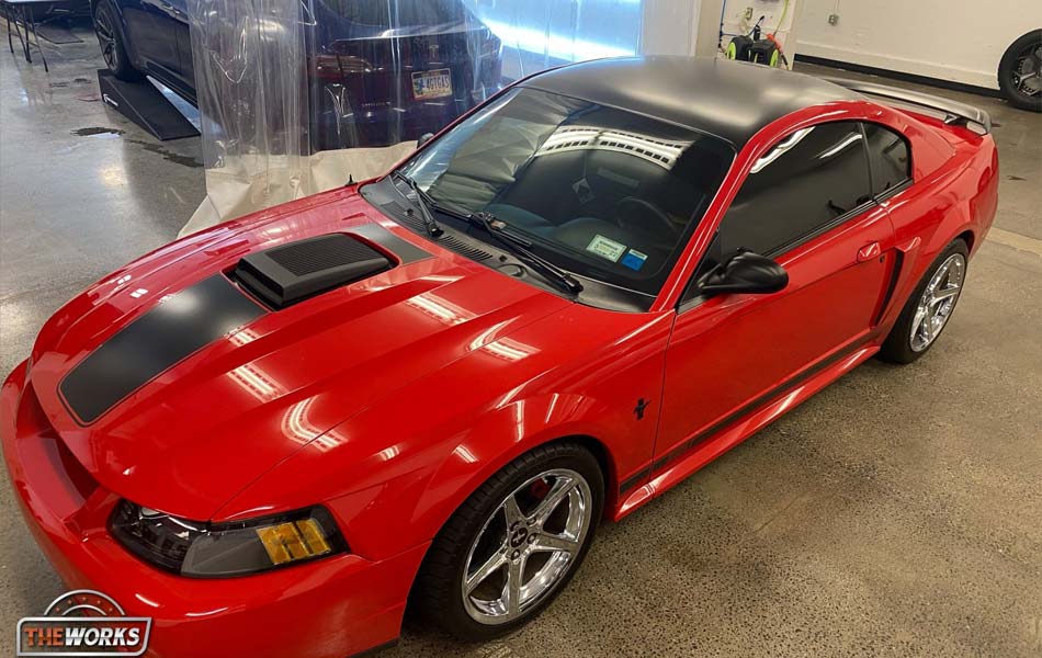 A red mustang with a black hood is parked in a garage.