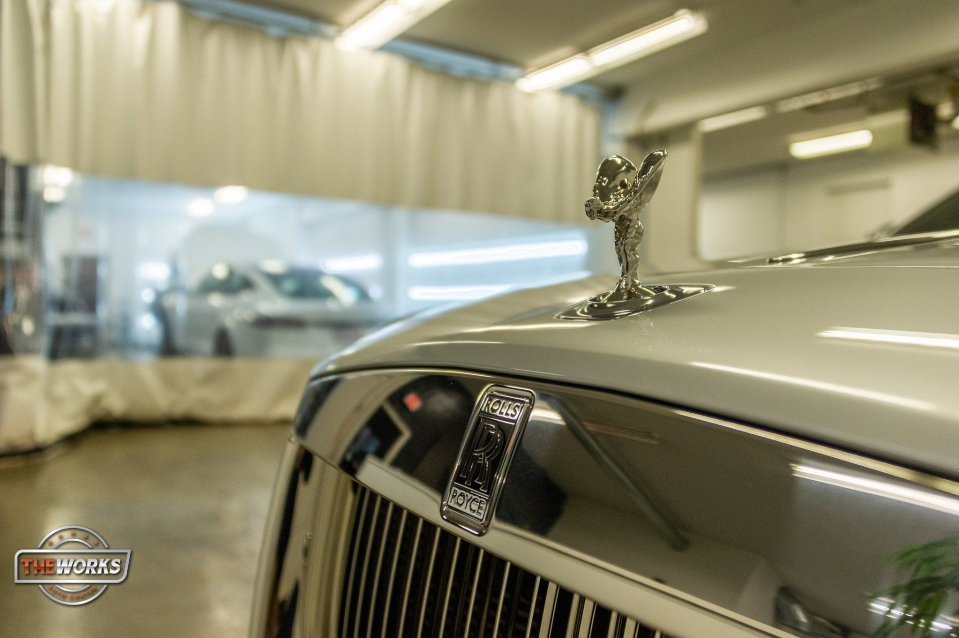 A close up of the hood of a silver rolls royce in a garage.