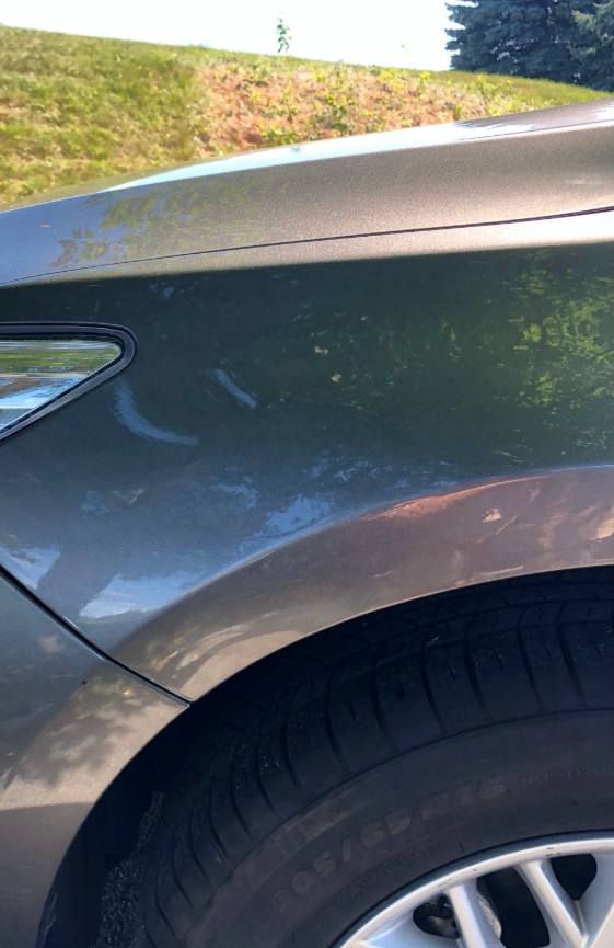 Gray car fender with tire and a grassy background.