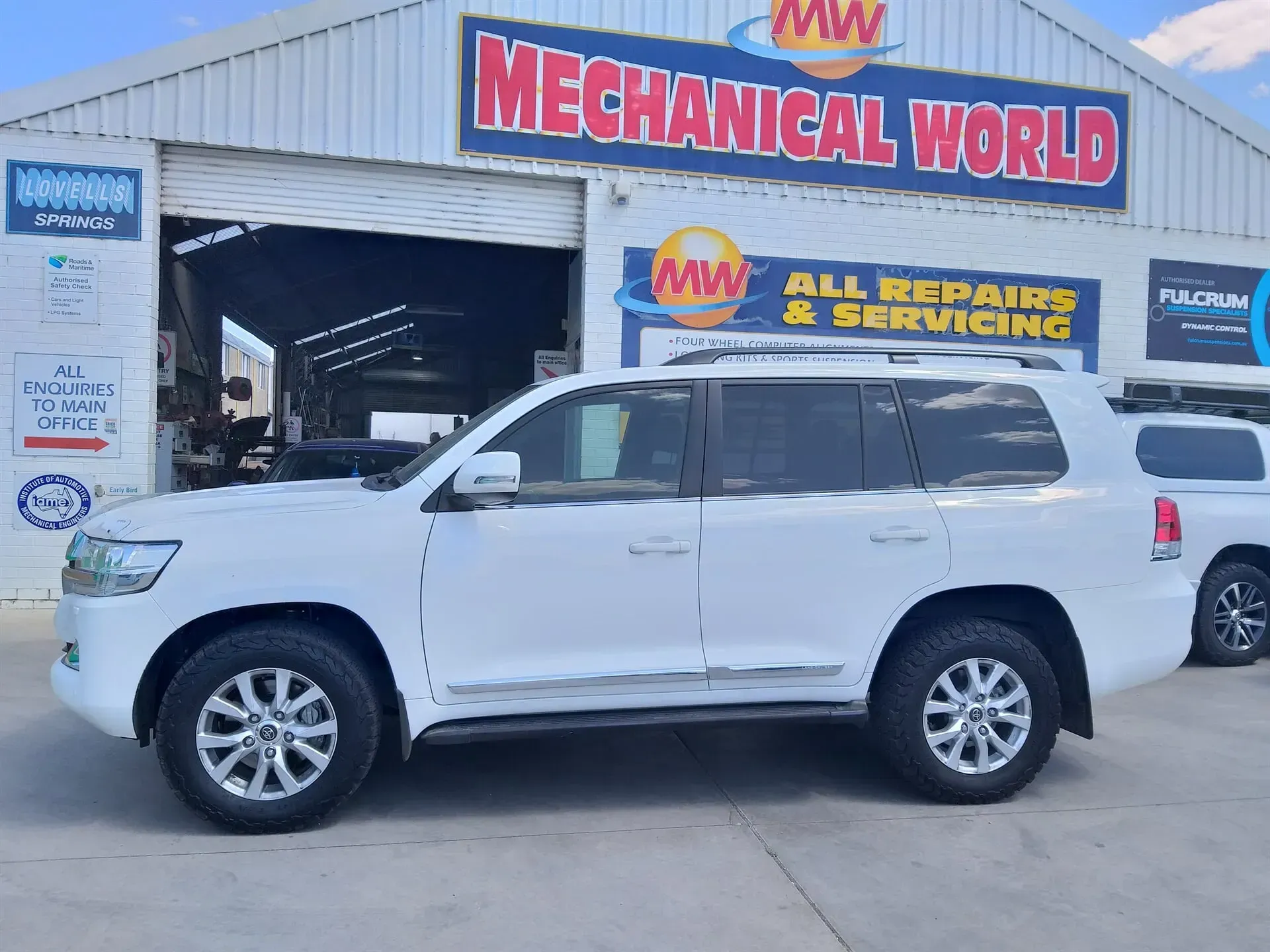 White Toyota Land Cruiser SUV parked in front of an auto repair shop
