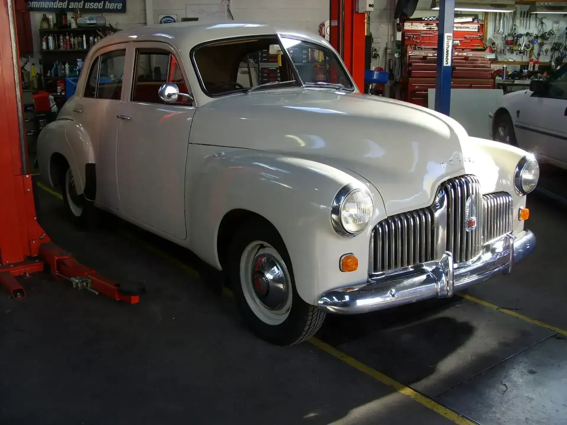 An Old White Car is Sitting on a Lift in a Garage — Mechanical World In Wagga Wagga, NSW