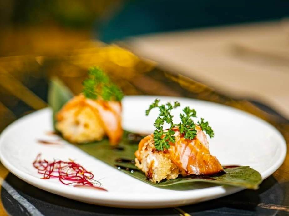 Piatto di sushi con salmone scottato, guarnizione di prezzemolo e condimento su un piatto bianco.