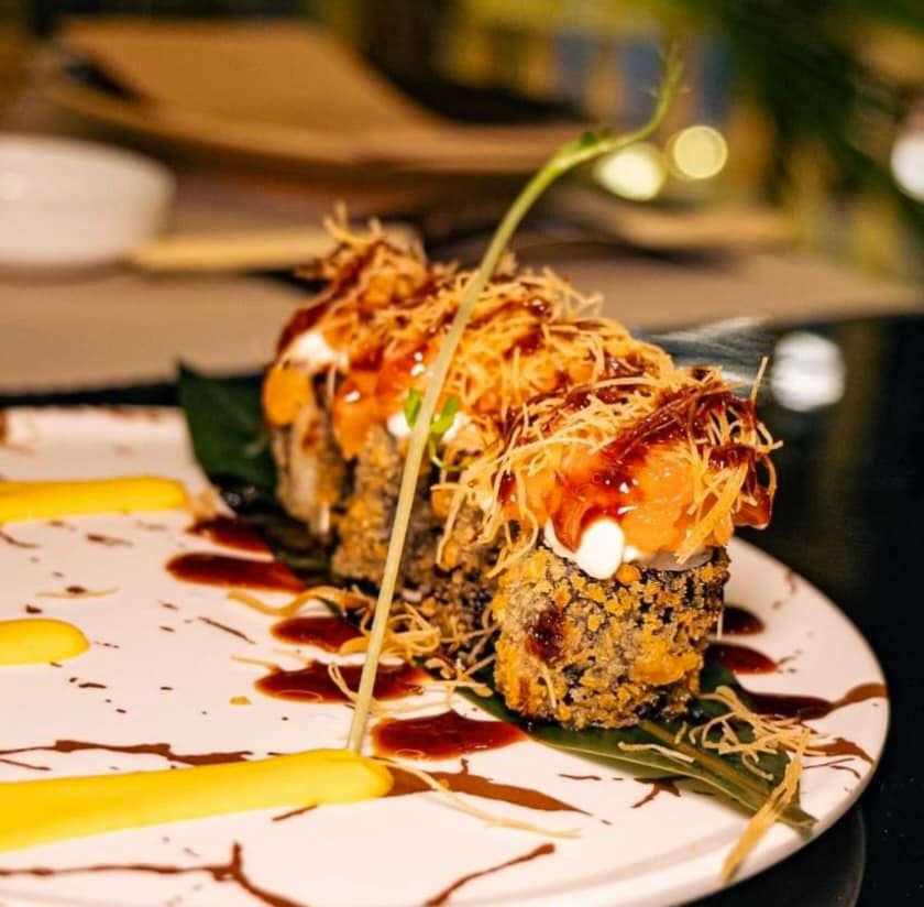 Rotolo di sushi con salmone, salsa e croccante guarnizione su un piatto con mango.