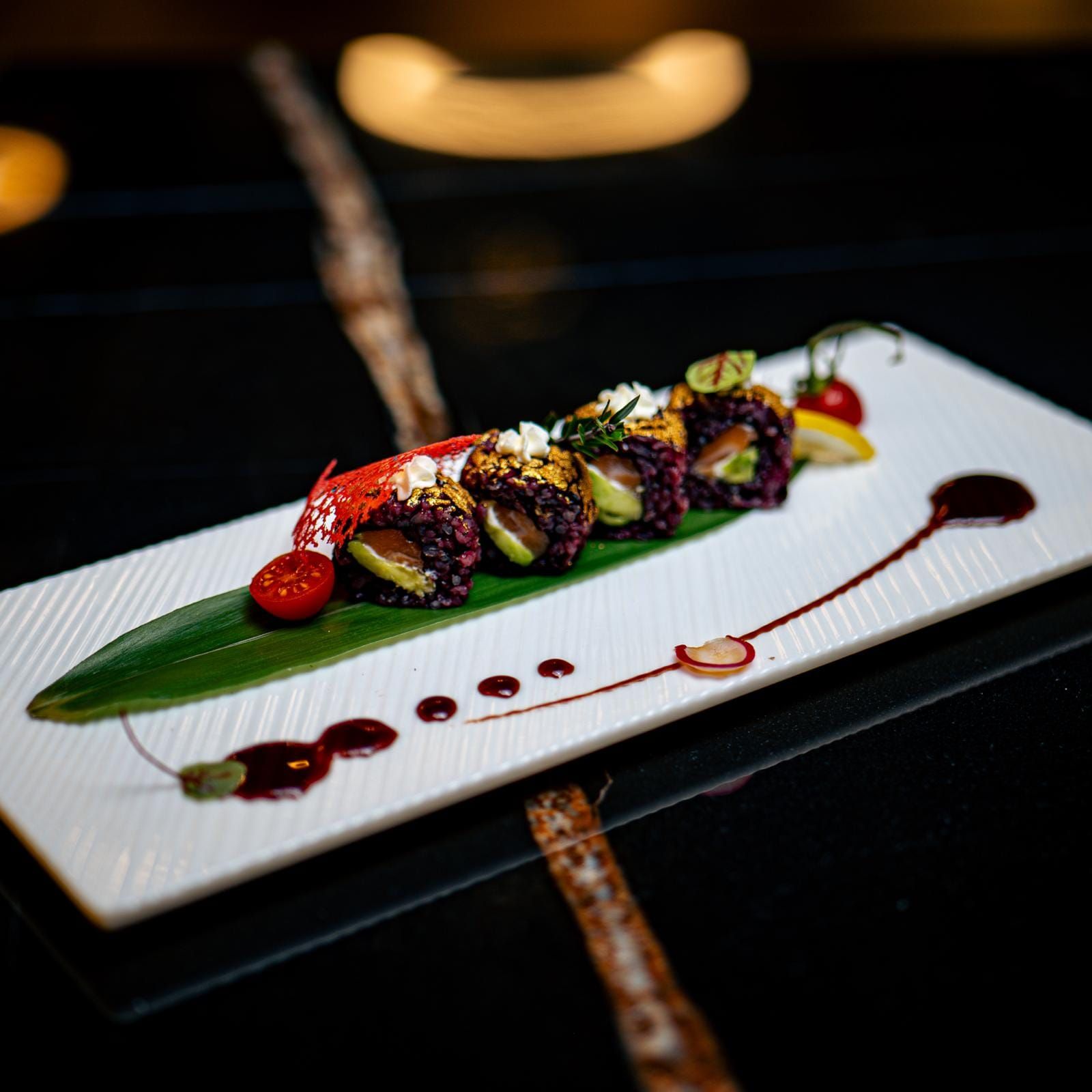 Rotolo di sushi su un piatto bianco con salsa e guarnizione. Riso nero, avocado e pesce all'interno.